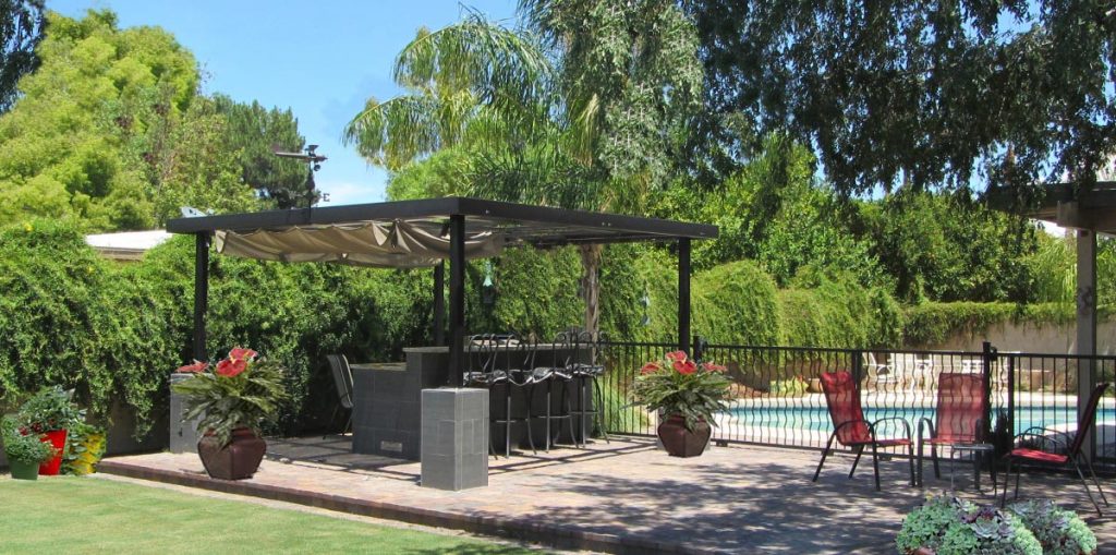 Photo: a vine-covered wall encloses a backyard shaded by lush trees and a canopy.