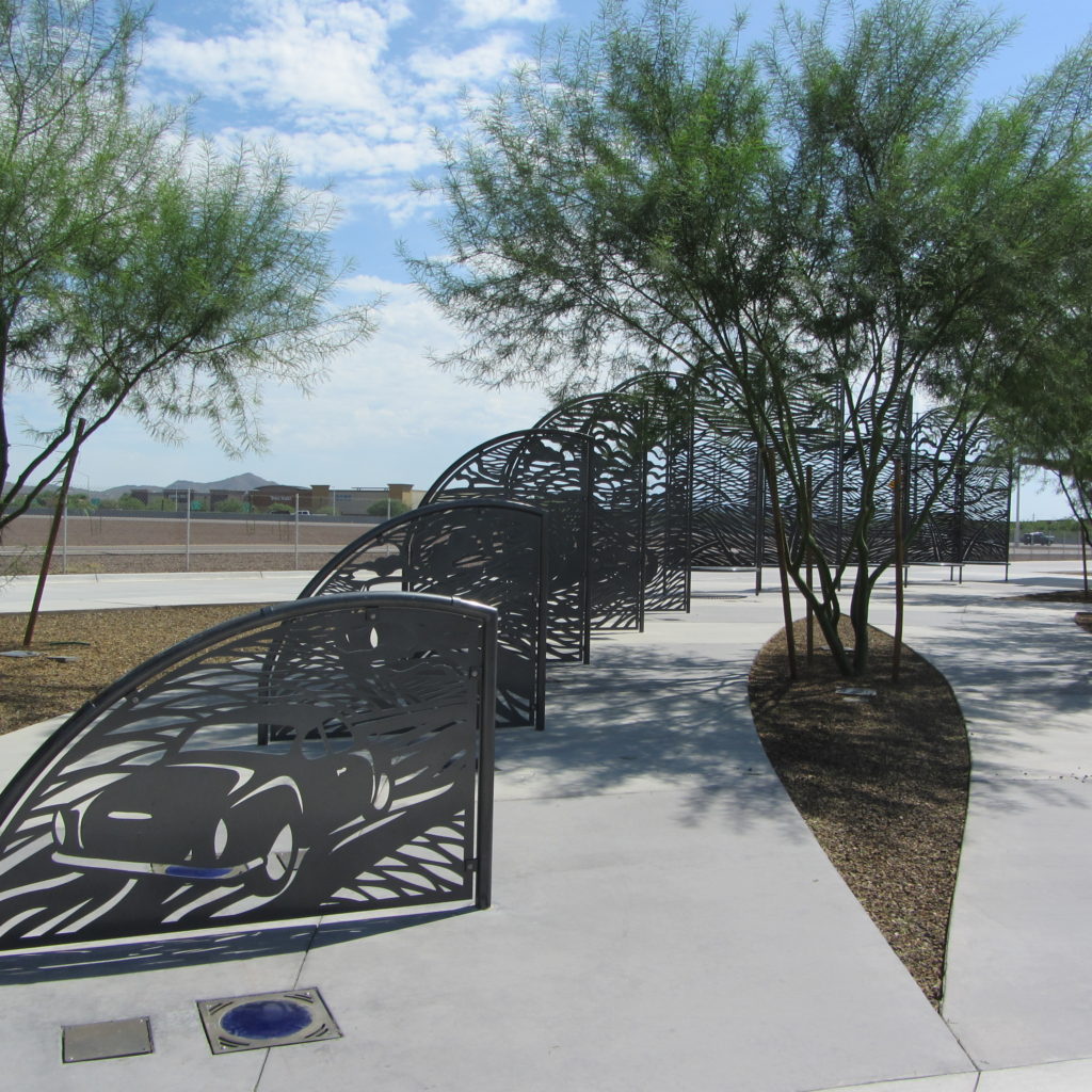 Photo of laser-cut metal art panels along a curving sidewalk shaded by palo verde trees